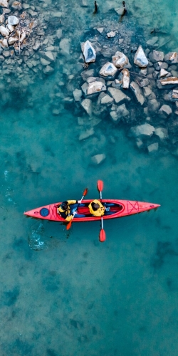 two athletic man floats on a red boat in calm blue waters river