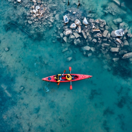 two athletic man floats on a red boat in calm blue waters river